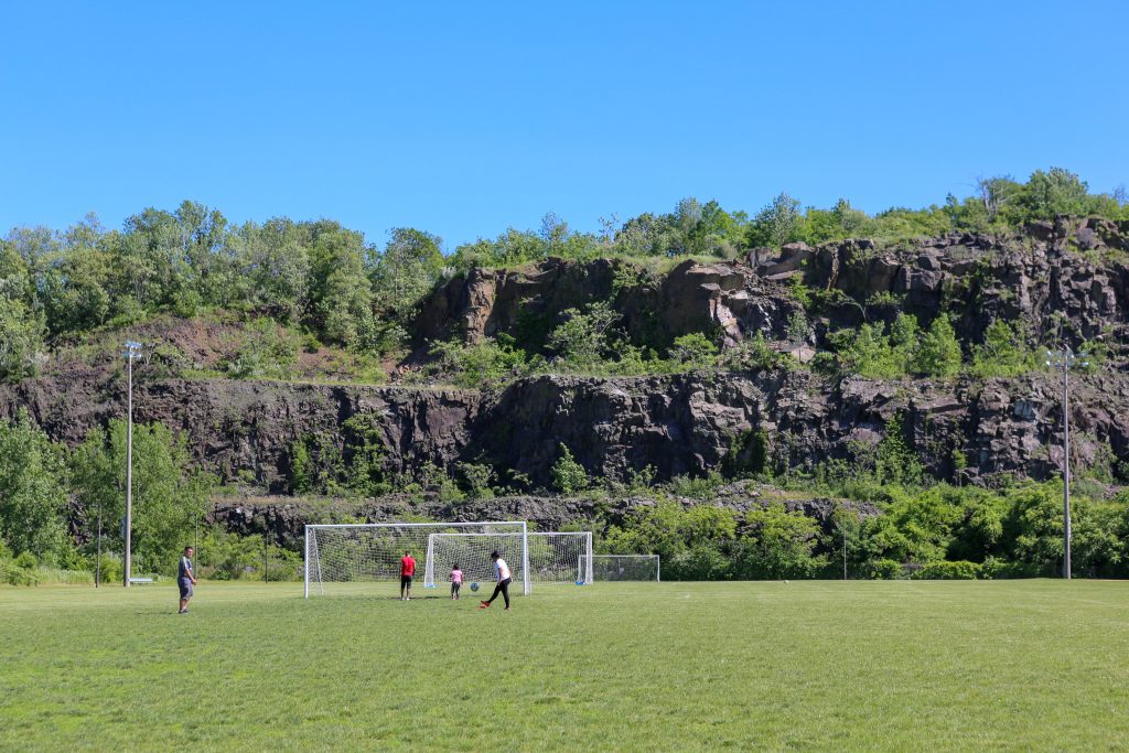 Soccer players on a field near a rocky hillside, highlighting outdoor recreational activities in the vicinity of Uforia Dispensary in Jersey City, NJ.