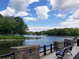 Scenic view of a calm lake surrounded by greenery and blue skies, with a park bench in the foreground, illustrating nearby recreational areas for Uforia Dispensary customers in North Bergen, NJ.