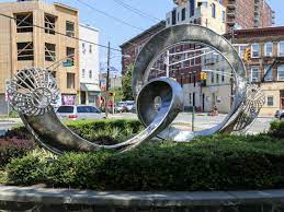 Sculptural installation featuring swirling metallic forms, surrounded by greenery, located near Union City, NJ, highlighting community landmarks and enhancing the area’s aesthetic appeal.