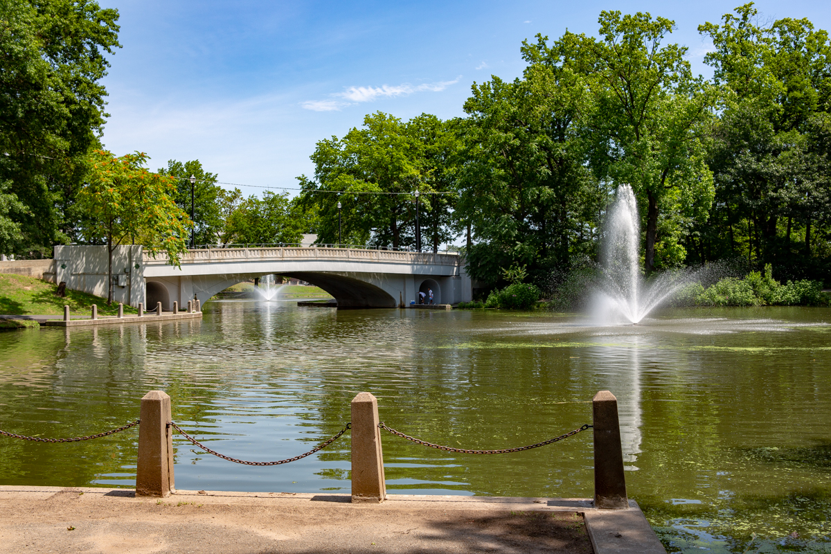 West Hudson Park view featuring a fountain in the pond, surrounded by lush greenery and a bridge, highlighting the community's natural beauty near Kearny, NJ.