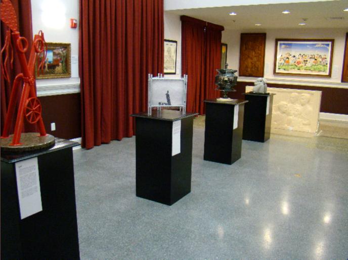 Art exhibition featuring various sculptures on display in a gallery with red curtains and framed artwork on the walls.