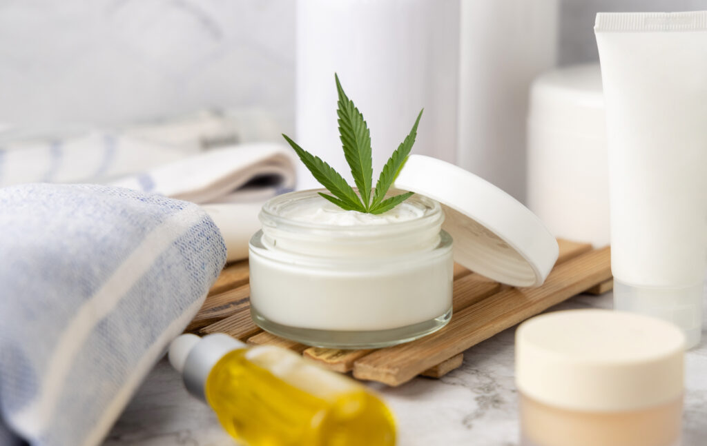 Opened cream jar with cannabis leaves, surrounded by skincare products, emphasizing THC pain relief cream for joint pain relief.