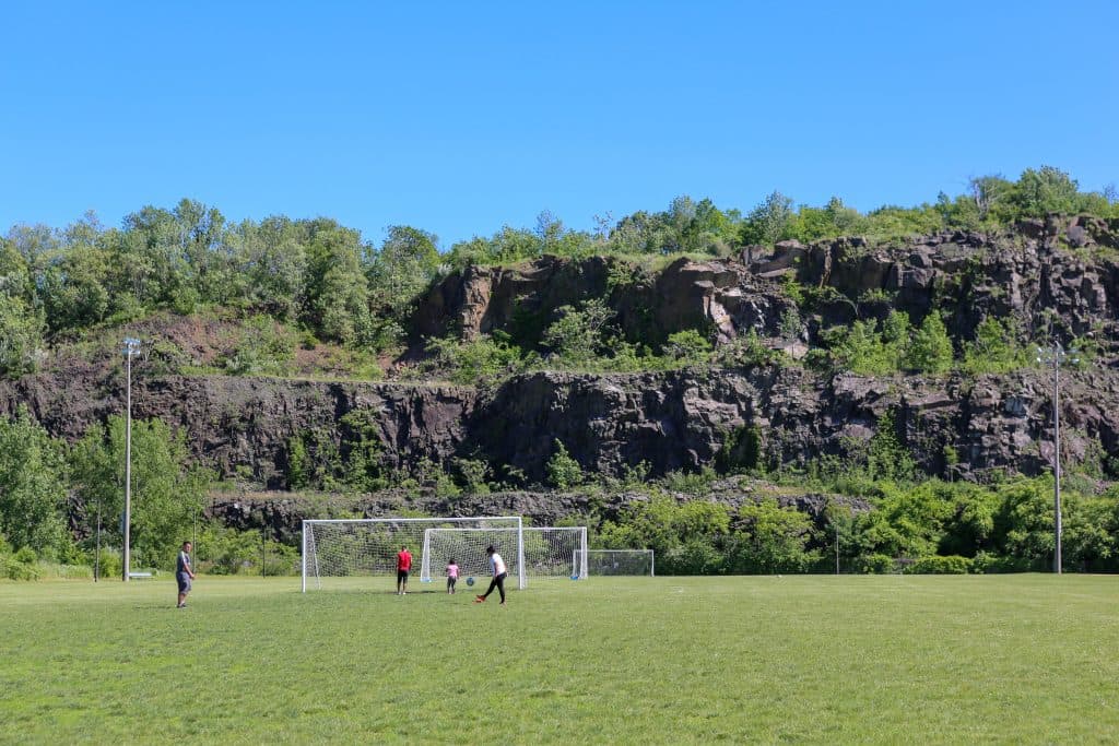 Soccer field at Laurel Hill Park with players practicing, surrounded by greenery and rocky cliffs, emphasizing outdoor recreational activities near Secaucus, NJ.