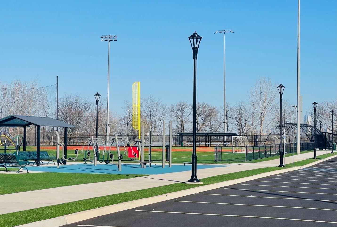 Park area featuring exercise equipment and sports fields, with lamp posts and green grass, located near Kearny, NJ, emphasizing community fitness and outdoor activities.