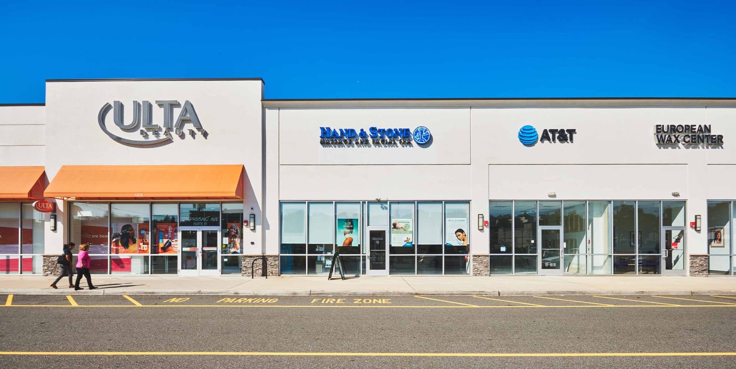 Kearny Commons shopping plaza featuring Uforia Dispensary, AT&T, Hand & Stone Massage, and European Wax Center, with clear blue sky and pedestrians walking by.