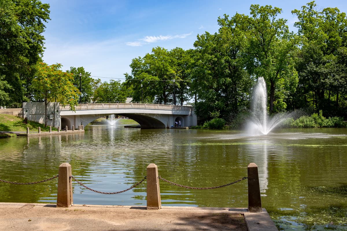 Bridge over a pond in West Hudson Park, featuring fountains and surrounded by lush greenery, near Uforia Dispensary in Kearny, NJ.