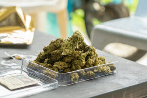 A clear container filled with green cannabis buds on a table